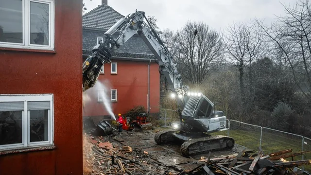 Bagger neben einem teilweise zurückgebauten Ziegelgebäude